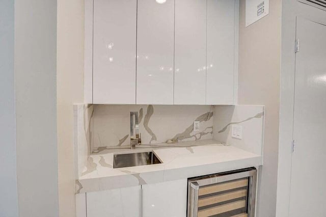 interior space featuring sink, beverage cooler, light stone counters, and white cabinetry