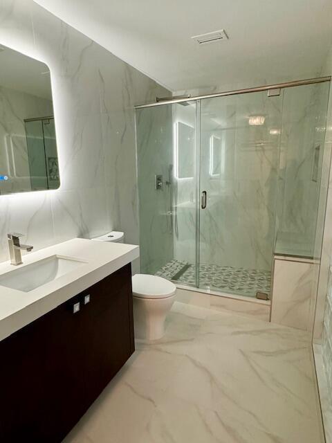 bathroom featuring toilet, a shower with door, tile walls, and vanity