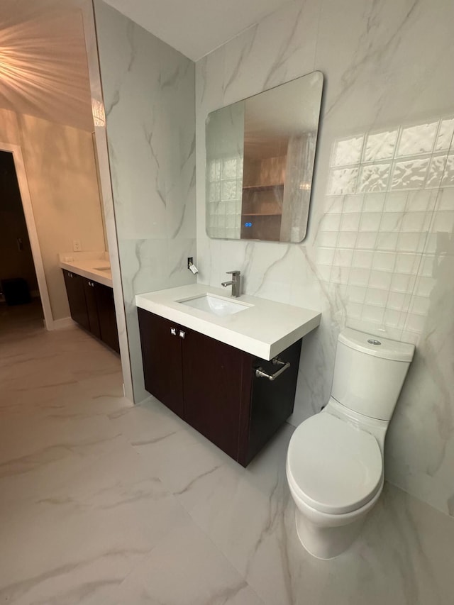 bathroom with marble finish floor, toilet, tile walls, and vanity