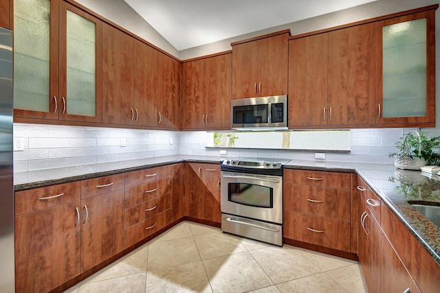 kitchen featuring lofted ceiling, backsplash, dark stone countertops, appliances with stainless steel finishes, and light tile patterned flooring