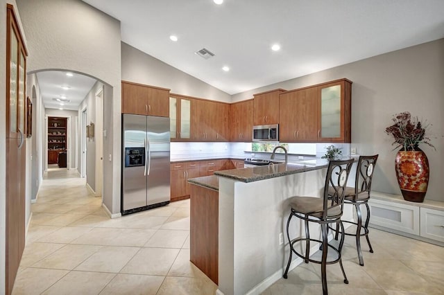 kitchen with stainless steel appliances, kitchen peninsula, dark stone counters, vaulted ceiling, and a kitchen bar