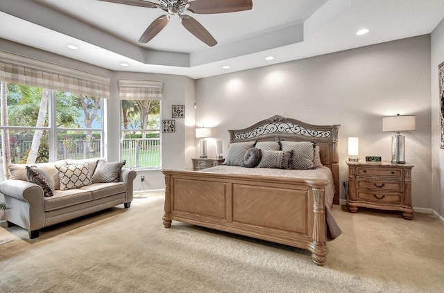 bedroom with light colored carpet, a raised ceiling, and ceiling fan