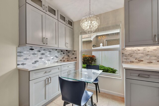 kitchen with pendant lighting, gray cabinets, light tile patterned floors, tasteful backsplash, and a chandelier