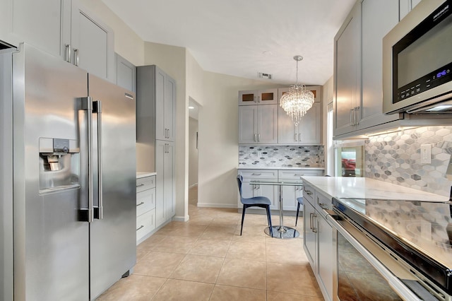 kitchen featuring appliances with stainless steel finishes, backsplash, gray cabinetry, hanging light fixtures, and light tile patterned flooring