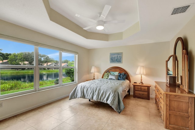 bedroom with ceiling fan, a water view, light tile patterned floors, and a tray ceiling