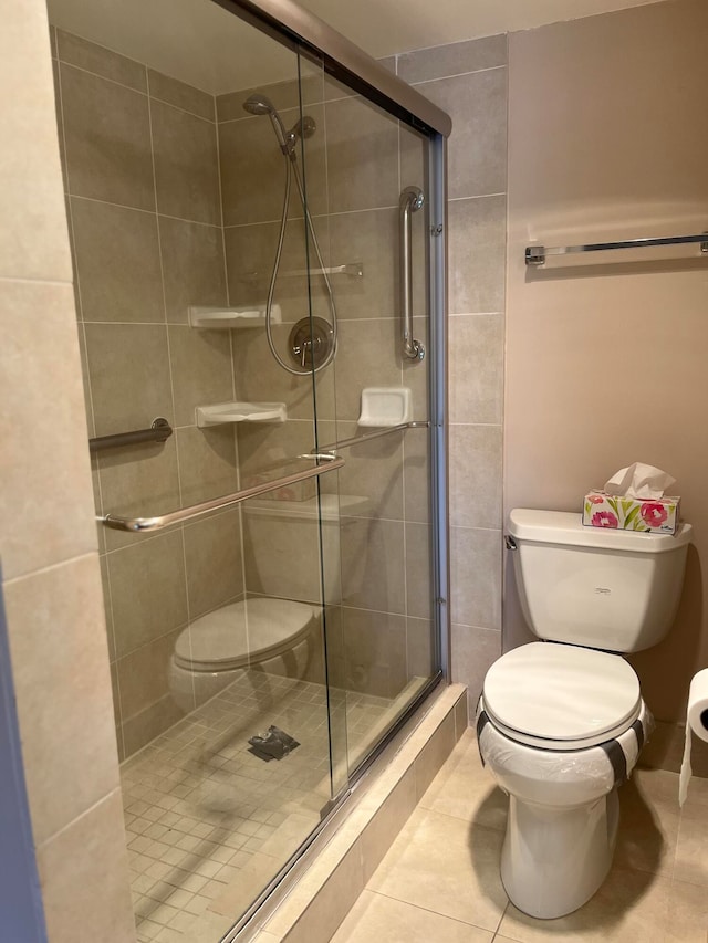 bathroom with tile patterned flooring, a shower with shower door, and toilet