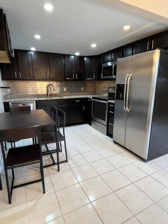 kitchen featuring tasteful backsplash, light stone countertops, sink, and appliances with stainless steel finishes