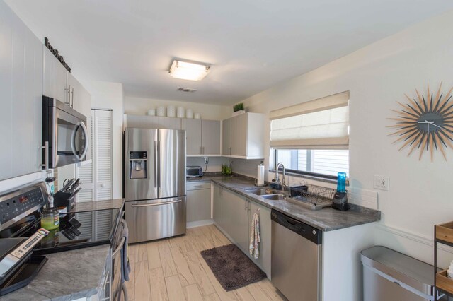 kitchen featuring appliances with stainless steel finishes, light wood-type flooring, gray cabinetry, and sink