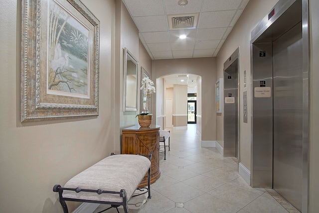 hallway featuring a paneled ceiling, elevator, and light tile patterned flooring