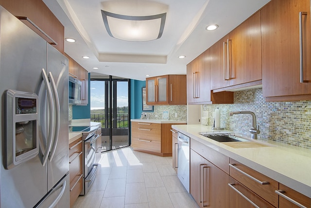 kitchen featuring a sink, light countertops, appliances with stainless steel finishes, decorative backsplash, and a tray ceiling