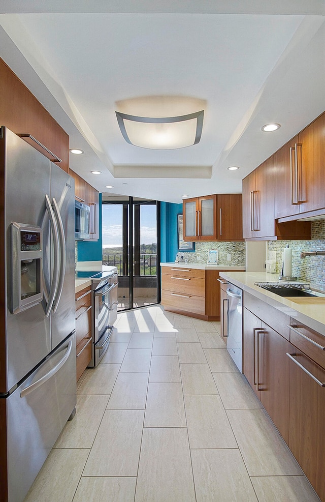 kitchen with appliances with stainless steel finishes, a tray ceiling, a sink, and tasteful backsplash