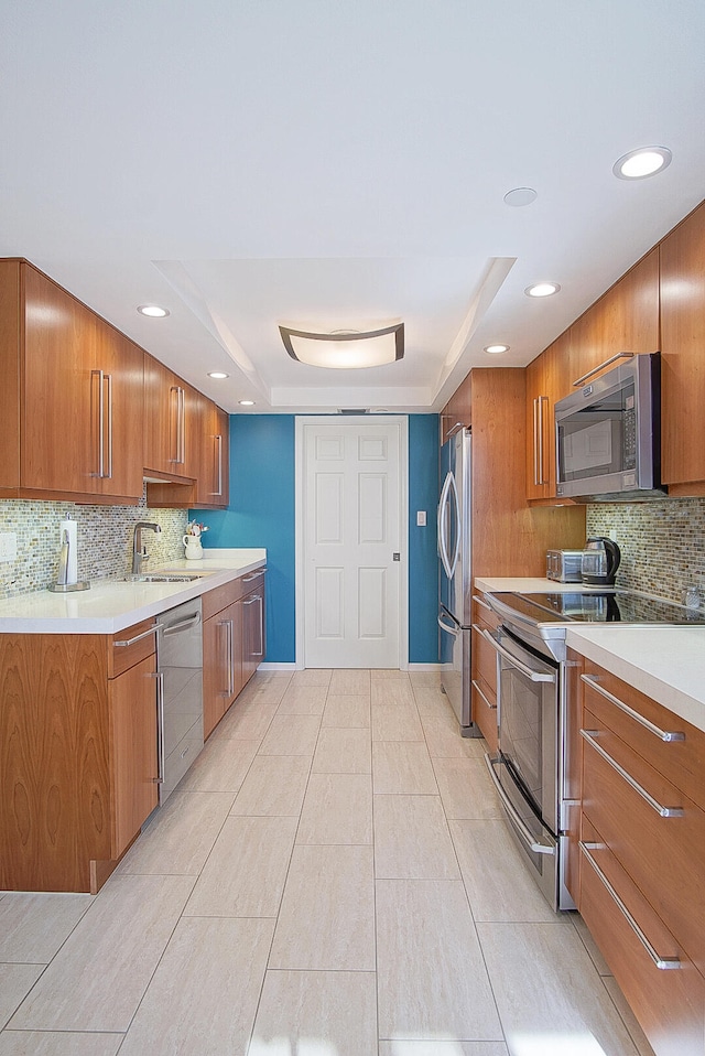 kitchen with brown cabinets, light countertops, backsplash, appliances with stainless steel finishes, and a sink