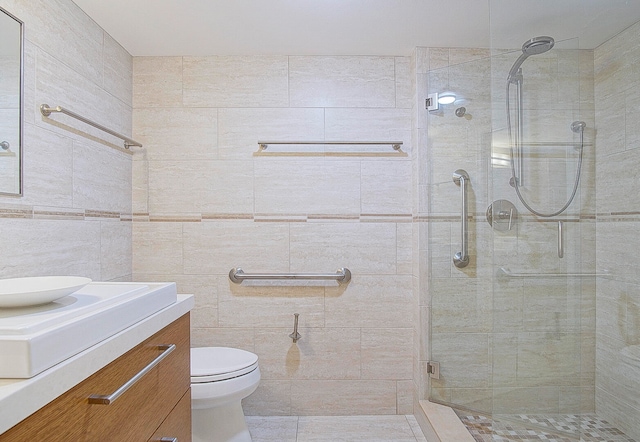 bathroom featuring vanity, a shower with door, toilet, and tile walls