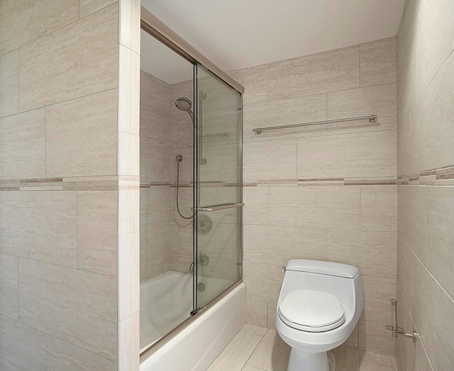 bathroom with toilet, combined bath / shower with glass door, and tile walls