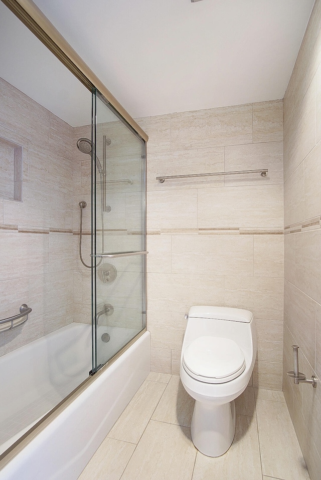 bathroom featuring tile patterned floors, toilet, combined bath / shower with glass door, and tile walls