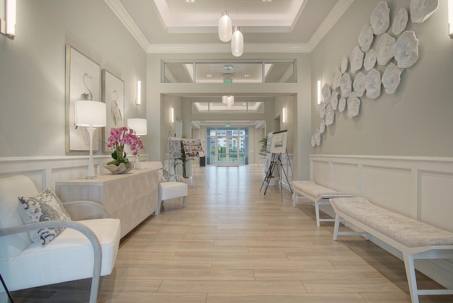 corridor with a raised ceiling, a wainscoted wall, ornamental molding, light wood-type flooring, and a decorative wall