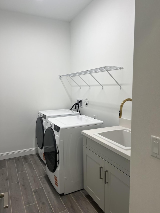 washroom with baseboards, wood finish floors, cabinet space, a sink, and washing machine and dryer