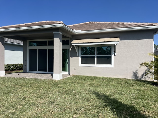 rear view of property featuring a lawn and stucco siding