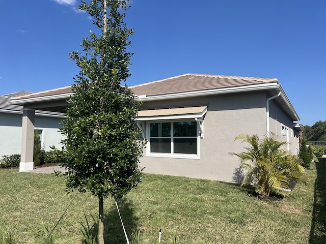 view of property exterior featuring a tile roof, a yard, and stucco siding