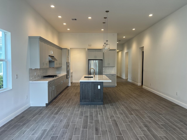 kitchen with gray cabinetry, under cabinet range hood, a sink, gas cooktop, and stainless steel fridge