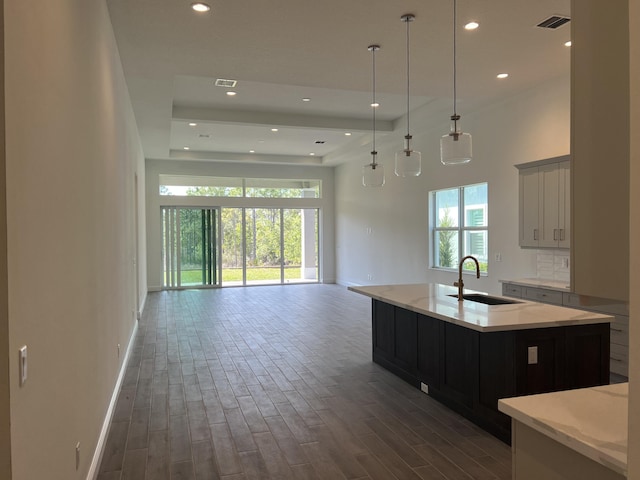 kitchen featuring visible vents, a sink, open floor plan, wood finished floors, and a kitchen island with sink