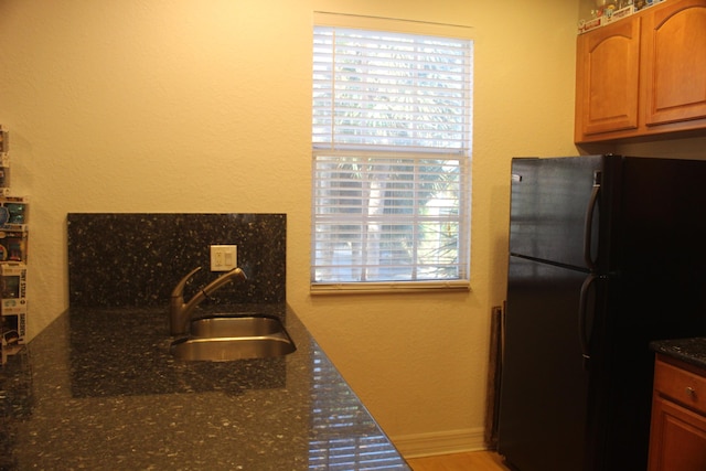 kitchen featuring dark stone countertops, black fridge, and sink