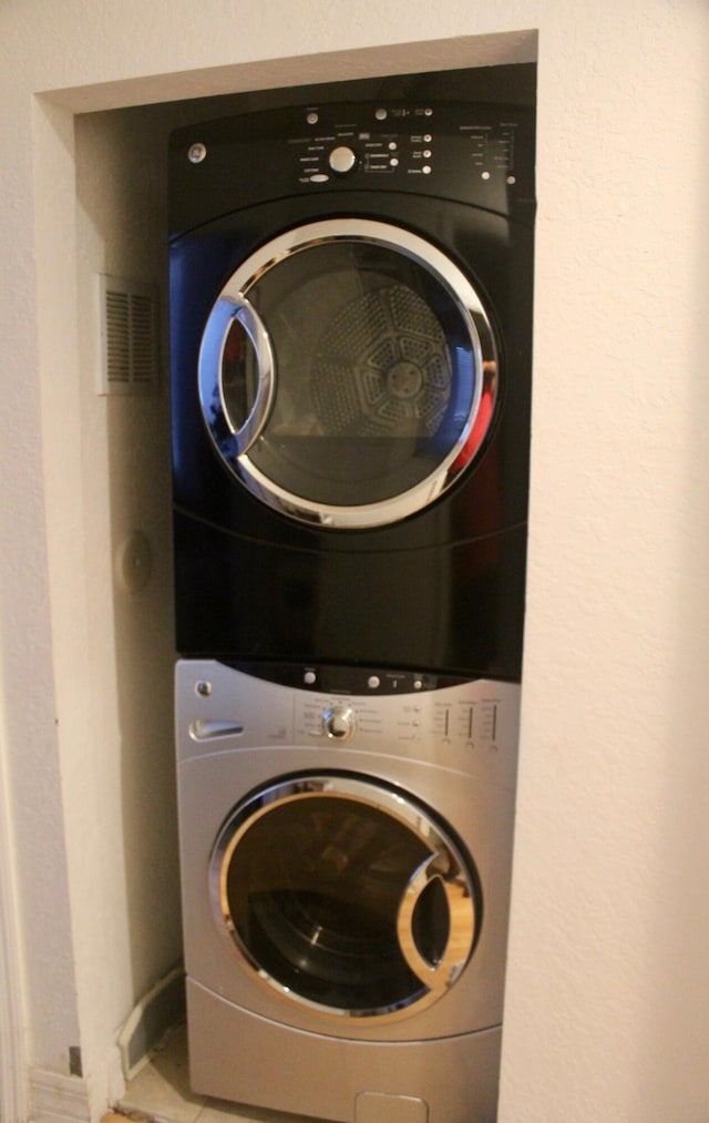 clothes washing area with tile patterned floors and stacked washer and dryer