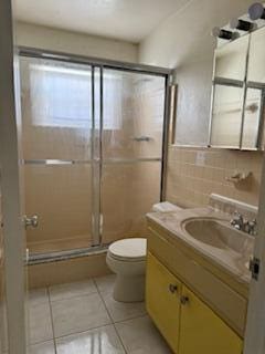 bathroom featuring vanity, tile patterned flooring, toilet, tile walls, and a shower with shower door