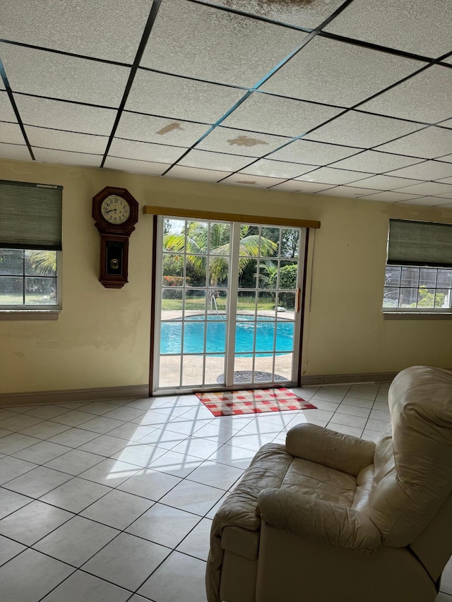 unfurnished living room featuring a drop ceiling, light tile patterned flooring, and a healthy amount of sunlight