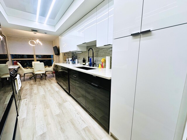 kitchen featuring tasteful backsplash, sink, white cabinets, light stone counters, and light wood-type flooring