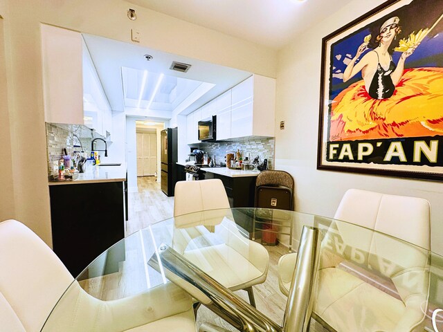 kitchen featuring white cabinets, backsplash, hanging light fixtures, electric range, and light hardwood / wood-style flooring