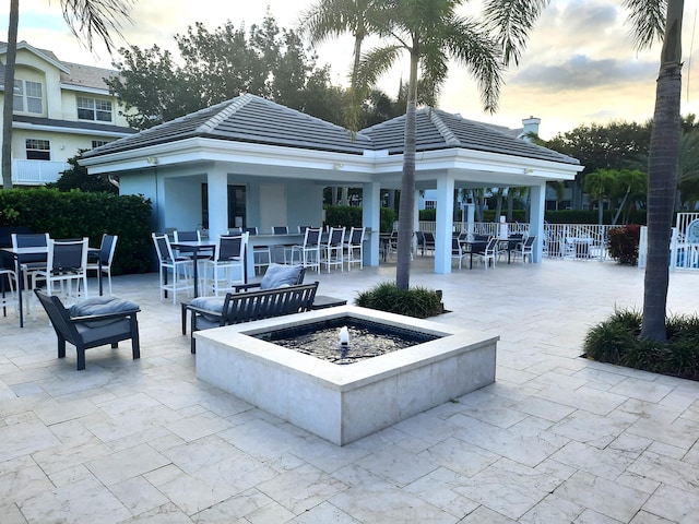 patio terrace at dusk with a gazebo, an outdoor fire pit, and exterior bar