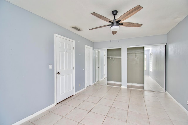 unfurnished bedroom with light tile patterned floors, ceiling fan, and multiple closets