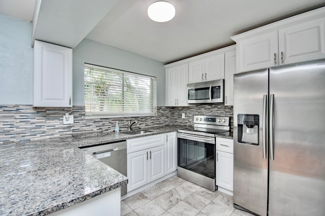 kitchen with light stone countertops, appliances with stainless steel finishes, tasteful backsplash, sink, and white cabinets