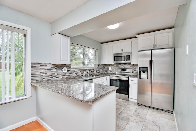 kitchen with white cabinets, appliances with stainless steel finishes, kitchen peninsula, and plenty of natural light