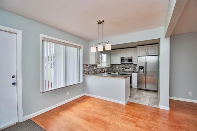 kitchen with kitchen peninsula, tasteful backsplash, stainless steel appliances, pendant lighting, and light hardwood / wood-style floors