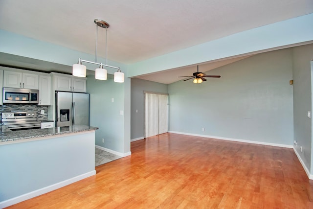 kitchen with backsplash, stone counters, hanging light fixtures, light wood-type flooring, and appliances with stainless steel finishes