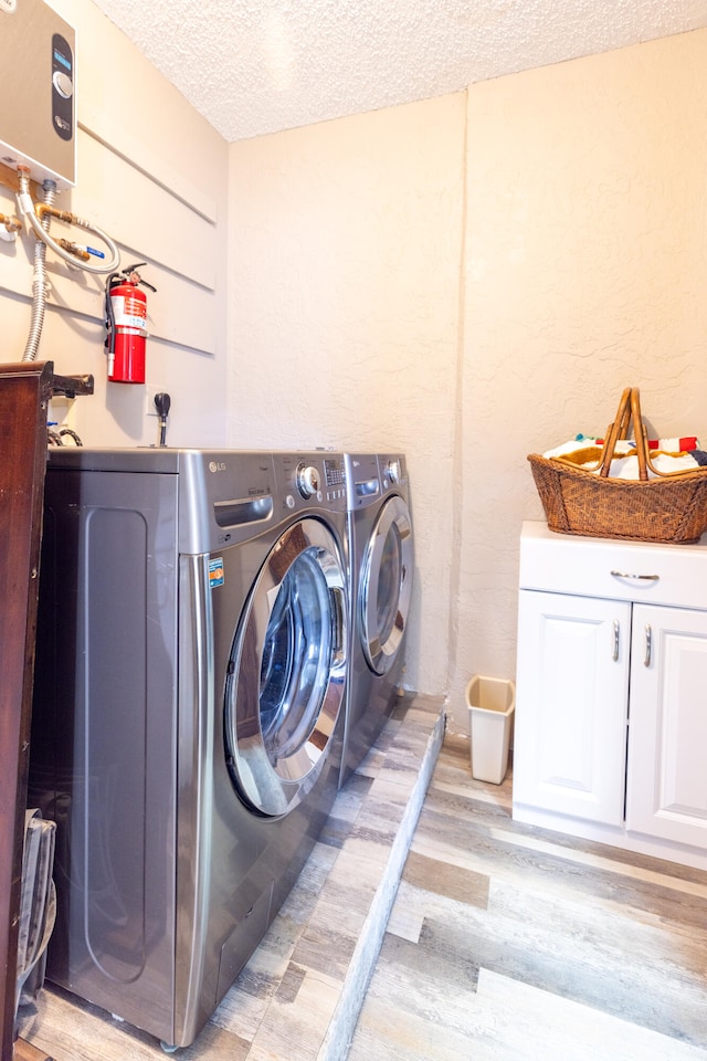 washroom with cabinets, light wood-type flooring, a textured ceiling, and separate washer and dryer