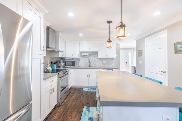 kitchen with white cabinets, hanging light fixtures, wall chimney exhaust hood, appliances with stainless steel finishes, and a kitchen island