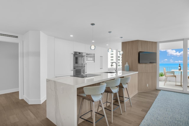 kitchen with white cabinets, light wood-type flooring, sink, and hanging light fixtures