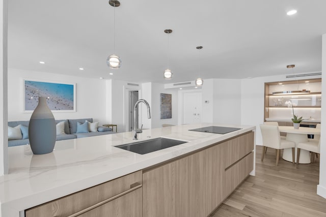 kitchen featuring light stone countertops, black electric stovetop, sink, light hardwood / wood-style floors, and hanging light fixtures