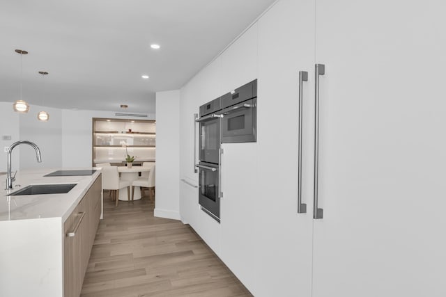 kitchen featuring pendant lighting, white cabinets, sink, light hardwood / wood-style flooring, and light stone counters