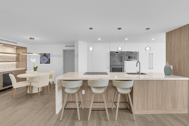 kitchen featuring stainless steel double oven, beverage cooler, sink, light hardwood / wood-style flooring, and hanging light fixtures