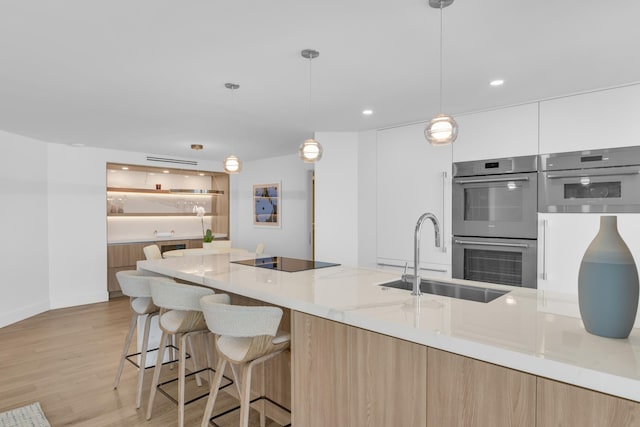 kitchen featuring white cabinets, hanging light fixtures, light hardwood / wood-style flooring, double oven, and light stone counters