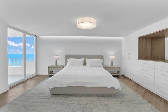 bedroom featuring a water view, wood-type flooring, a wall of windows, and access to outside