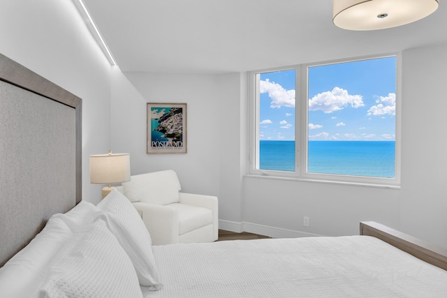 bedroom with hardwood / wood-style flooring and a water view