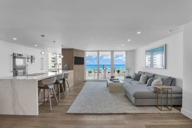 living room featuring a wall of windows, light hardwood / wood-style flooring, a water view, and sink