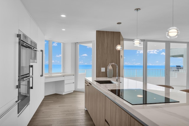 kitchen with sink, white cabinets, light hardwood / wood-style floors, black electric cooktop, and a water view