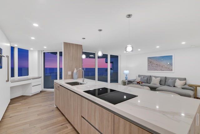 kitchen featuring pendant lighting, black electric stovetop, sink, light hardwood / wood-style flooring, and light stone countertops