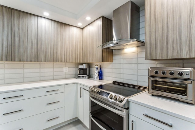 kitchen with double oven range, decorative backsplash, white cabinets, and wall chimney exhaust hood